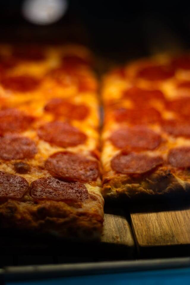 Detroit-style pepperoni pizza with thick crust, crispy edges, melted cheese, and cupped pepperoni slices on a dark surface