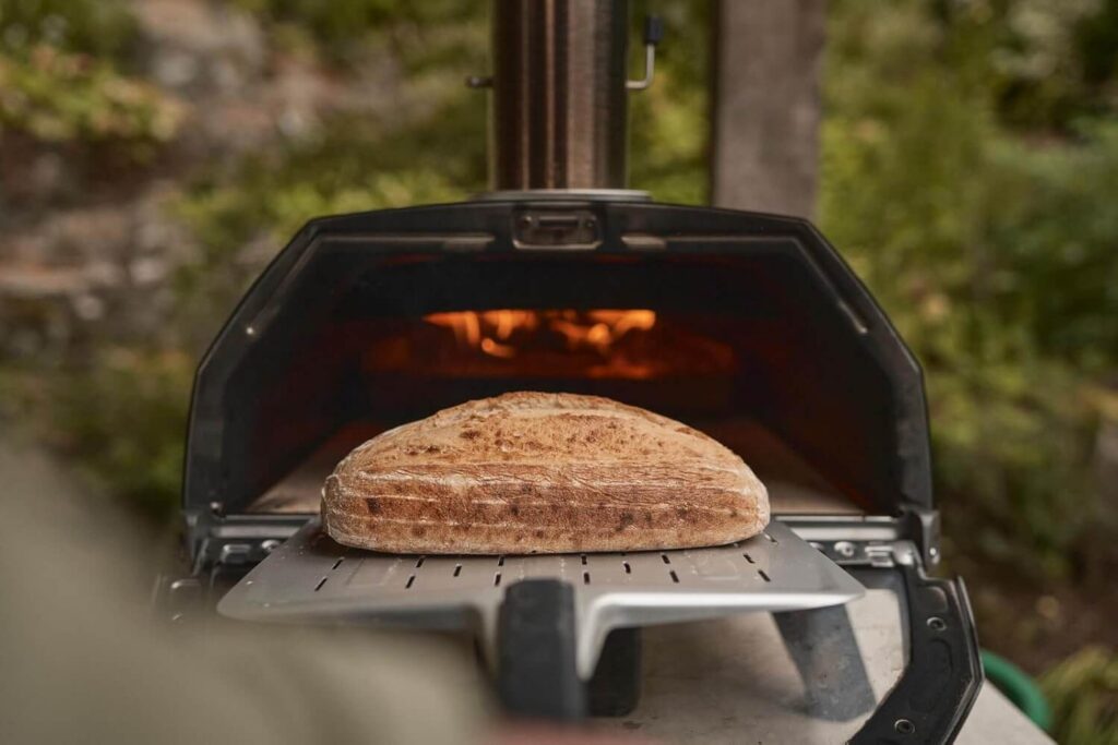 Freshly baked artisan bread being pulled from an Ooni Karu 2 Pro pizza oven with a pizza peel.