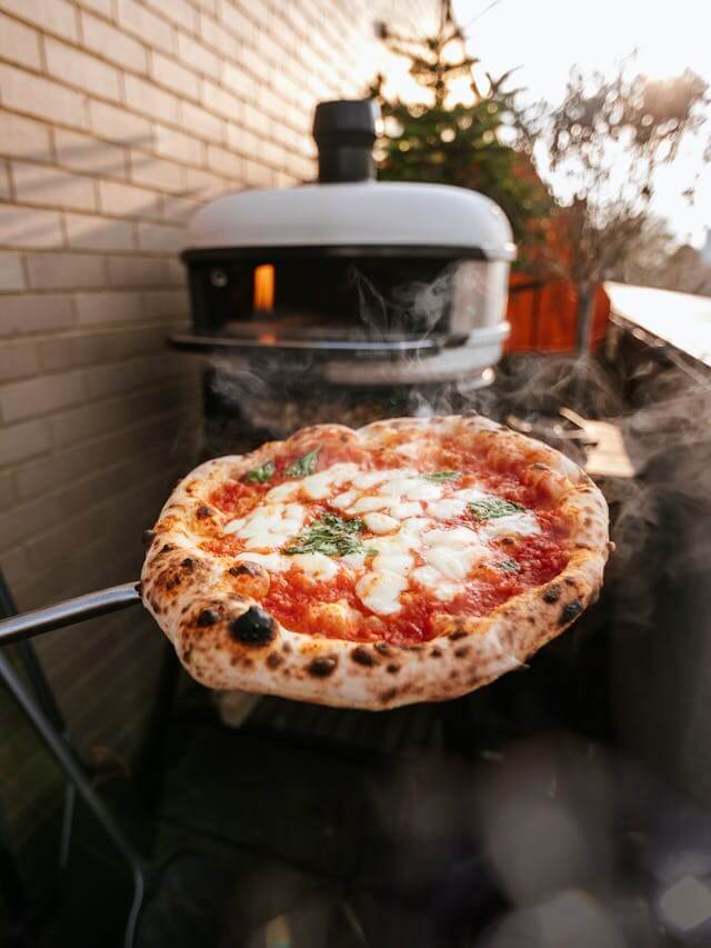 Freshly baked Neapolitan Margherita pizza with melted cheese and basil taken out of a Gozney Dome oven