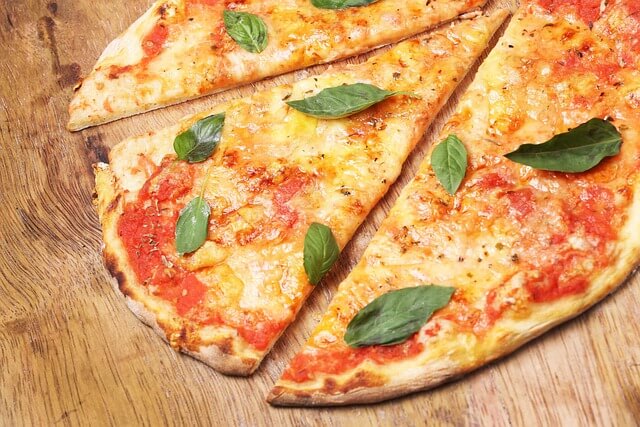 New York style pizza slices with cheese, tomato, and basil on a wooden board