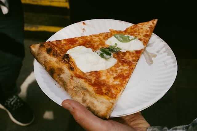 Close-up of a classic New York pizza slice with tomato sauce, mozzarella, and fresh basil served on a paper plate