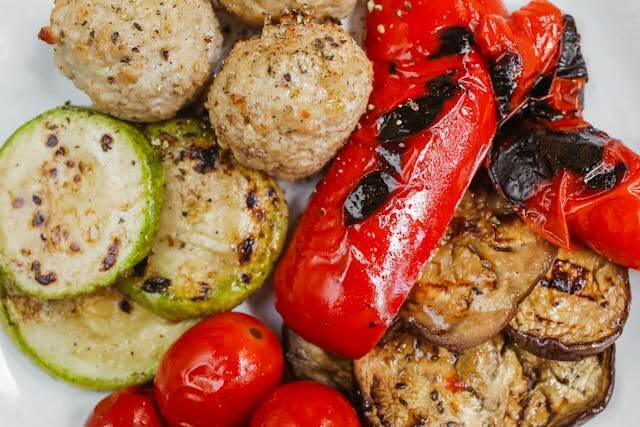 A close-up shot of a plate of grilled vegetables, including sliced zucchini, roasted red bell peppers, and grilled eggplant