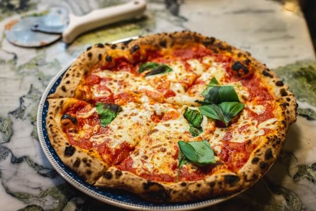 Authentic Neapolitan Margherita pizza on a plate, topped with melted fresh mozzarella, San Marzano tomato sauce, basil leaves, and a charred puffy crust.