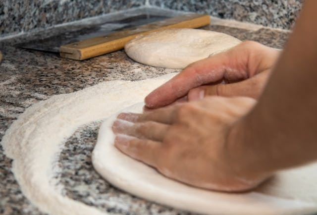 pizza dough being shaped on a floured surface before baking