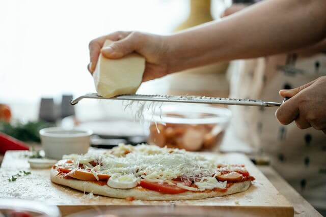Grating cheese onto pizza to improve topping balance before baking