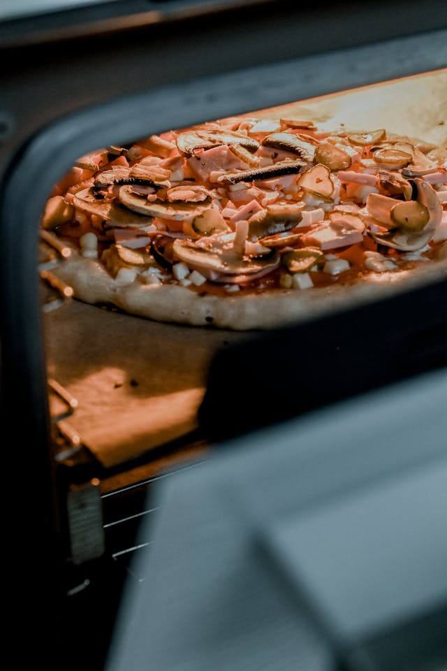 Pizza baking on a tray inside a home oven with toppings