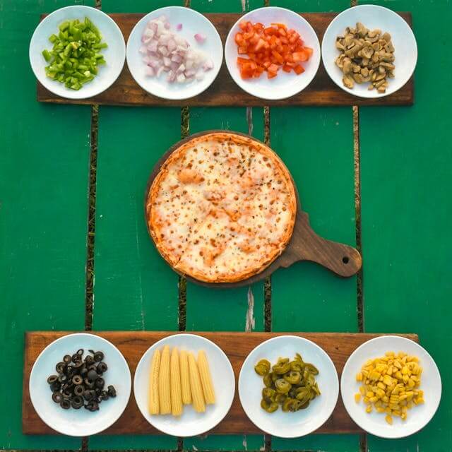 Pizza dough with various toppings like vegetables, cheese, and meats on a table before baking