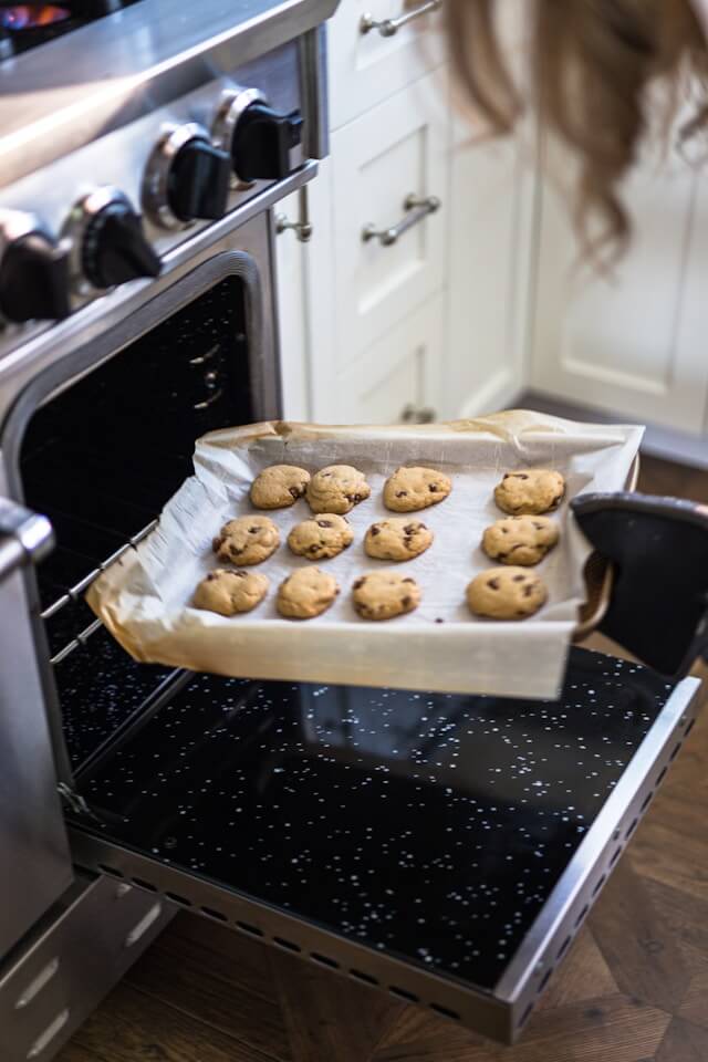 Tray of golden chocolate chip cookies being pulled out of the oven after baking