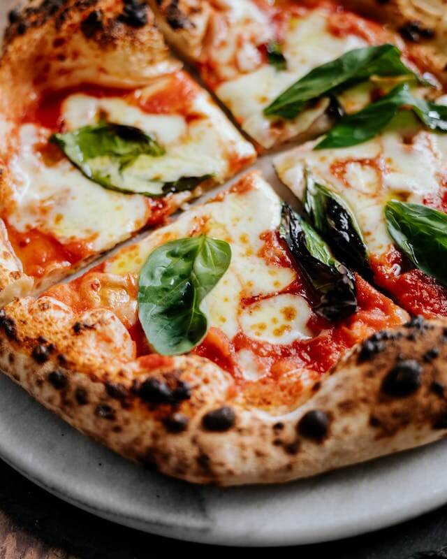 Close up of leopard spots on a Neapolitan pizza crust with fresh basil and mozzarella