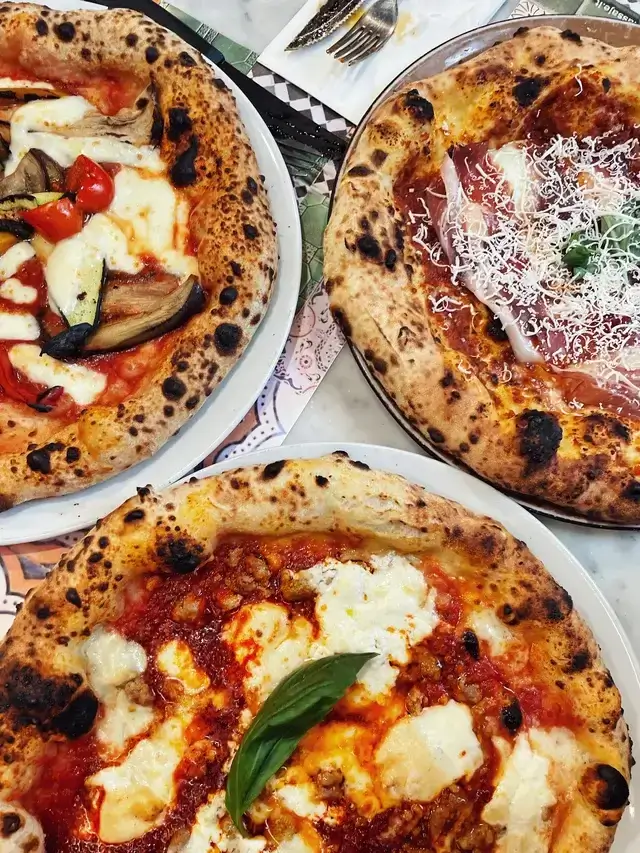 Three Neapolitan pizzas showing classic leopard spots on the crust