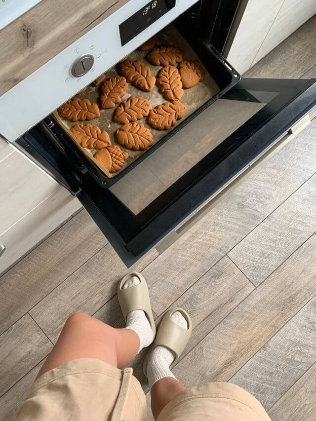 A person standing in front of an open oven looking at a tray of baked leaf-shaped cookies
