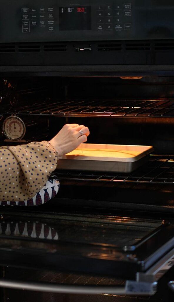 Hand reaching into an open oven to test a cake with a toothpick